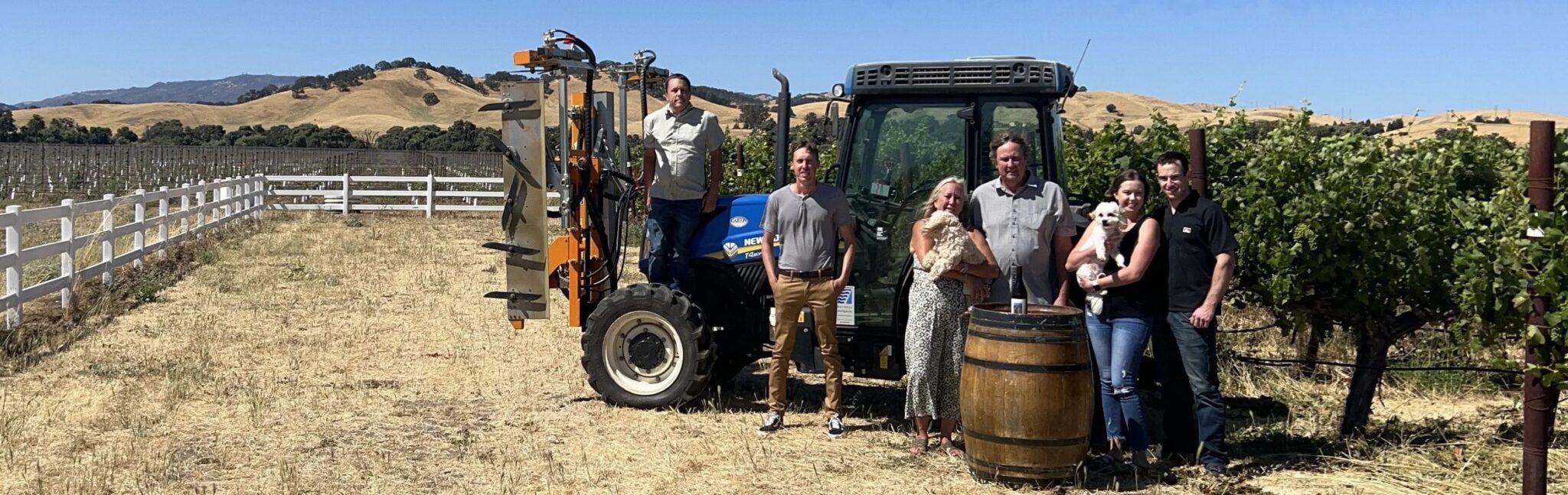 The Andrews family standing with their dogs, a tractor, and an oak barrel in the Abernathy Lane vineyard